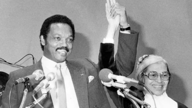 Jesse Jackson standing next to Rosa Parks while holding her hand in front of the press. Image courtesy of Getty Images.
